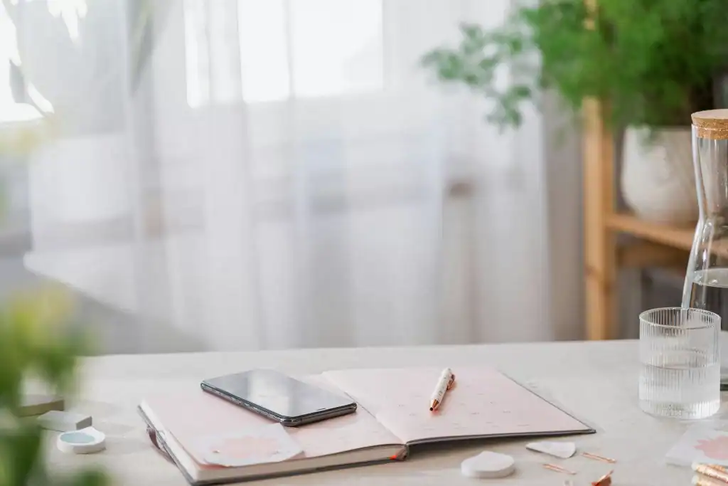 SEO-Strategie planen: Notizbuch, Stift und Smartphone auf Tisch, daneben Wasserglas – Symbolbild für fokussierte SEO-Vorbereitung im Ranking Ready Paket